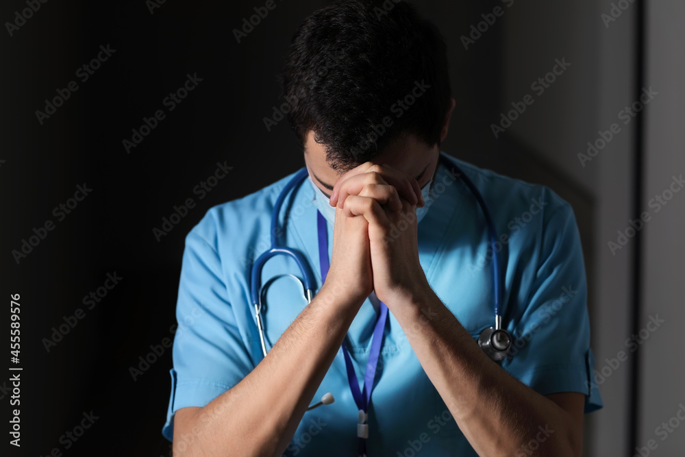 Praying male doctor on dark background