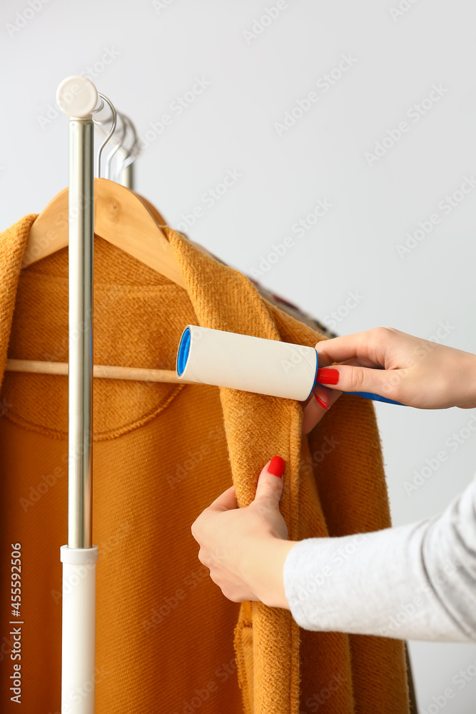 Woman cleaning coat with lint roller on light background
