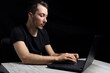 Young male programmer with laptop on black background in low or dark key.