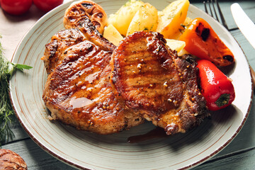 Plate with tasty pork steaks and grilled vegetables on color wooden background, closeup