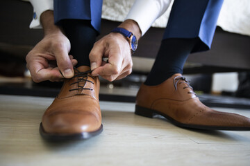 Wall Mural - Closeup of a male in elegant clothing tying his brown leather shoes