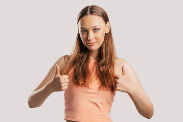 beautiful young girl smiling and shows thumbs up gesture with two hands on a white isolated backgrou