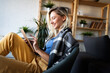 © NDABCREATIVITY - Relaxed young woman in sofa smiling content, happy and reading, working on tablet pc at home