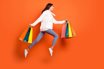 Wall Mural - Full length body size view of beautiful cheerful girl jumping carrying new things running isolated bright orange color background