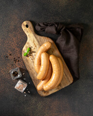 Wall Mural - Pork sausages on a serving wooden board on a dark culinary background top view