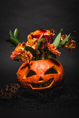 Wall Mural - orange flowers in spooky and carved pumpkin on black background