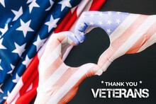 Veterans Day. Man's Hands In Gloves The Color Of The American Flag, Showing A Heart Gesture. Black Background With Flag. Close Up. The Concept Of National American Holidays