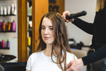 Canvas Print - Master woman hairdresser gently curls hair curling girl in a beauty salon. Hair styling