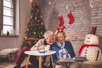 Wall Mural - Senior couple drinking coffee and looking through old photo album on Christmas day