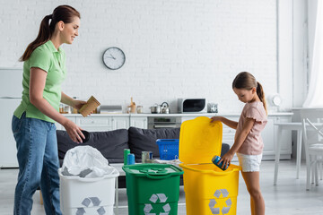 Wall Mural - Smiling woman looking at daughter with tin can near bin with recycle sign in kitchen