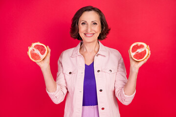 Wall Mural - Photo of old slimming retired lady hold two grapefruit slice wear pink jacket isolated red color background