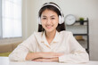 © Chanakon - Young asian woman wearing headphone look at camera video conference online sitting in living room at home. Business Woman look at screen Meeting on social media live steam. Work, learning from home.
