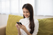 © Chanakon - Happy young asian woman looking at screen of smartphone sitting on sofa in living room she shopping online. She very happy. Teenage girl reading news from mobile phone feeling excited.
