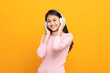 © Chanakon - Cheerful asian female teenager listen to the music with white headphone dancing on isolated yellow background. Beautiful young woman in hand touch a wireless headphone having fun with music.