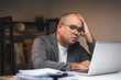 © Chanakon - Asian businessman working with laptop computer in the dark office at night. Indian man work hard overtime serious thinking hand on head. Feeling stressed and headache in warm light late at night