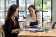 © amnaj - Team of young Asian businesswoman sitting at work brainstorming  analyze holding a notebook pen pointing at the document the laptop is placed on the office desk.