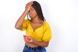 © Jihan - Upset depressed Young african american woman with braids over white wall makes face palm as forgot about something important holds mobile phone expresses sorrow and regret blames
