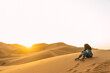 © Kike Arnaiz/Stocksy - woman sitting in sandy dunes in desert