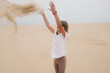 © Maria Manco/Stocksy - Portrait of young girl on sand dune, throwing sand in the air