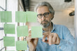 © Mihajlo Ckovric/Stocksy - Businessman writing notes on a stickers on a glass wall