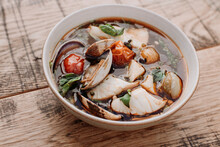 Bowl of spicy seafood soup on a rustic wooden table.