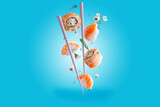 Fototapeta Maki - The concept of flying sushi. Rolls and sushi with salmon levitation with flowers and chopsticks on a blue background