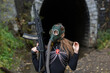 A woman in a black suit and gas mask with a machine gun in her hands