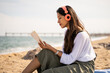 © Alba Vitta/Stocksy - Beautiful young woman relaxing reading book at beach