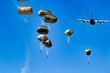 Military parachutist paratroopers parachute jumping out of a air force planes on a clear blue sky day.