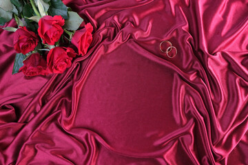 texture of luxury pink silk fabric, background with drapery for fashion design, gold wedding rings, copy space. bouquet red of roses, concept of congratulations on wedding day