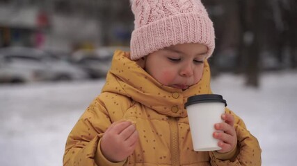 Wall Mural - Child girl drinking cocoa and eating cookie outdoors in winter snowy day. Happy childhood activities. Christmas holidays. Cold weather