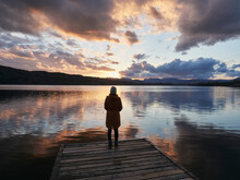 Female On A Jetty Watching The Sunset Over Lake Windermere. Lake District, UK.