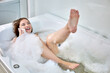 © grigvovan - Cute woman is having an emotional conversation on phone while lying in bathtub on bathroom.