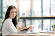 © NAMPIX - Portrait of young beautiful asian woman holding mug and book, smiling and looking at camera white sitting at the table.