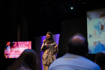 Wall Mural - Female speaker in hijab on stage talking to audience