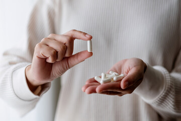 Closeup image of a woman holding and showing white medicine capsules in hand