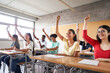 © CarlosBarquero - Multi-ethnic students in the classroom with hands raised. Smiling young people answering teacher's question.