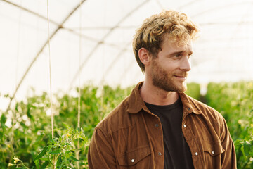 Wall Mural - Smiling organic farmer standing in a greenhouse