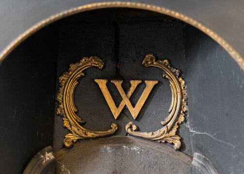 Large gold coloured letter W in fireplace of abandoned old grand house falling into disrepair.