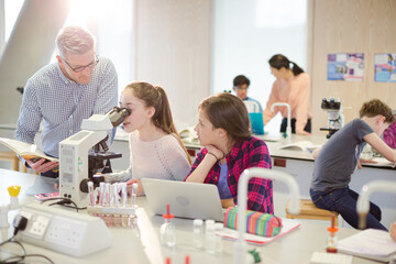 Wall Mural - male teacher helping girl students using microscope, conducting scientific experiment in laboratory 
