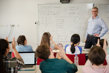 male teacher leading lesson at whiteboard in classroom