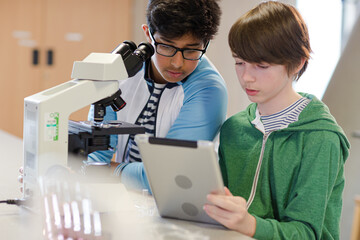 Wall Mural - focused boy students using digital tablet at microscope in laboratory classroom