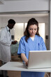 © DC Studio - Caucasian woman using laptop at desk in hospital ward for professional healthcare. Young adult with nurse occupation working as consultant for specialist, surgeon, medic, doctor
