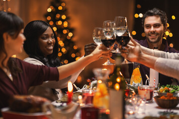 holidays, party and celebration concept - multiethnic group of happy friends having christmas dinner at home and drinking wine