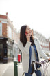 © KOTO - Smiling young woman commuting on bicycle, talking on cell phone on sunny urban street