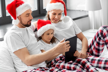 Poster - family, winter holidays and people concept - happy mother, father and little daughter with tablet pc computer in bed at home on christmas