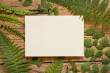 Blank Paper Card On A Wooden Table Decorated With Fern Leaves