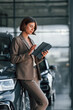 © standret - With tablet in hands. Woman is indoors near brand new automobile indoors