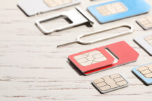 Different SIM Cards, Ejector And Tray On White Wooden Background, Closeup