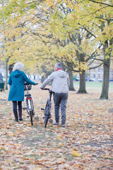 Wall Mural - Senior couple walking bicycles among trees and leaves in autumn park